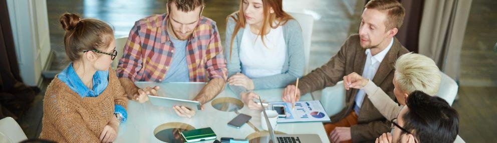 Vernetzen Es ist eine Gruppe von Studierende zu sehen die um einen Tisch herum sitzen und gemeinsam arbeiten.