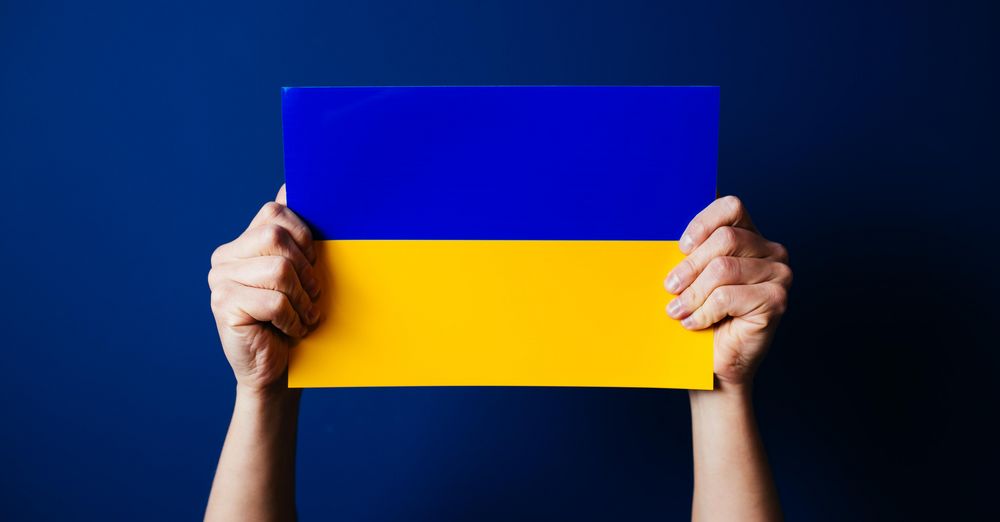 Zwei Hände halten eine kleine ukrainische Flagge in die Höhe.