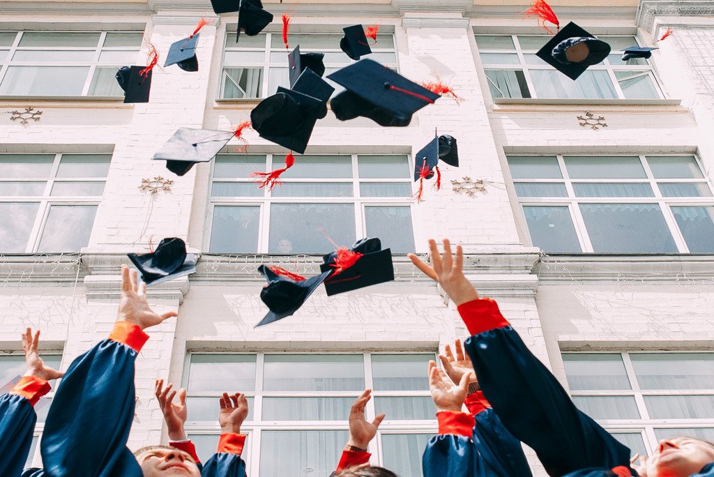 Das Bild zeigt die Arme von Studenten, die ihren Abschlusshut in die Luft werfen. 