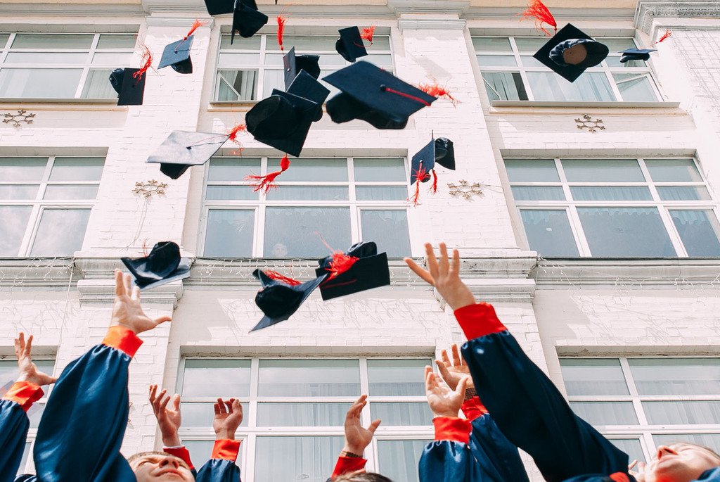 Das Bild zeigt die Arme von Studenten, die ihren Abschlusshut in die Luft werfen. 