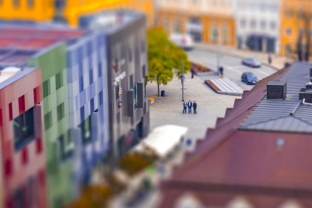 Das Bild zeigt eine Luftaufnahme der Passauer Stadtgalerie und auf ihrem Vorplatz drei Hochschullehrende der Universität Passau (Bild: Universität Passau).